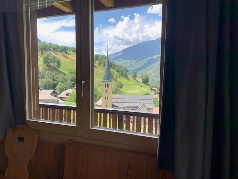 View from the chalet towards the church of Grengiols and the green mountain slopes.