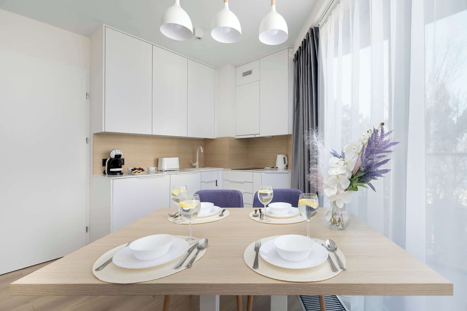 A bottle of wine and two glasses stand ready on the dining table, accompanied by a small decorative plant. The blurred background shows the clean lines of the kitchen and living area.