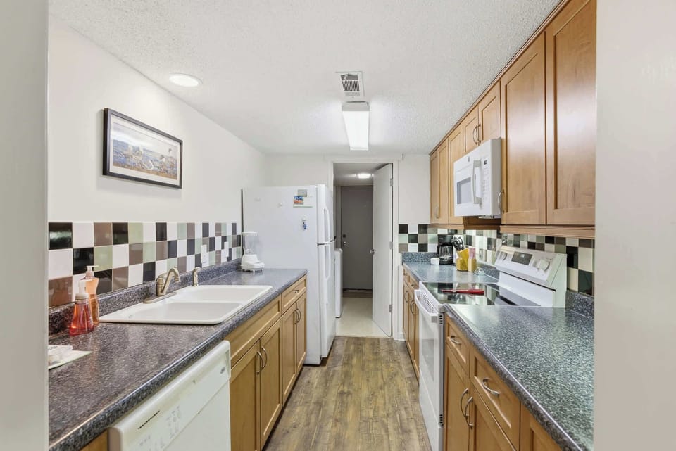 Checked tiling and oak cabinetry create a nostalgic, homey feel in this efficient kitchen. Bright overhead lighting illuminates the granite counters, making the space a cheerful and practical spot for preparing your favorite vacation meals.