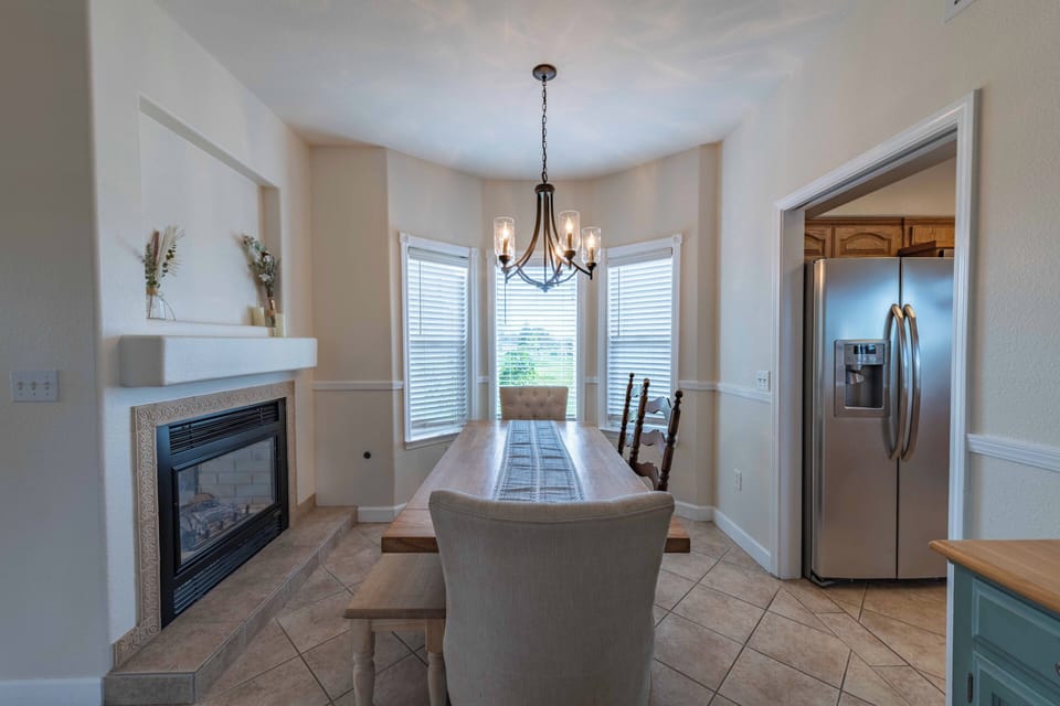 Gather around your elegant dining table by the warm fireplace, where memorable meals unfold beneath the graceful chandelier's glow.