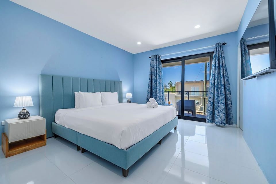 Our primary bedroom features sliding glass doors that lead to a private outdoor space, perfect for sipping coffee while the island wakes up. With minimalist decor and a striking upholstered headboard, it’s the ultimate blend of luxury and relaxation.