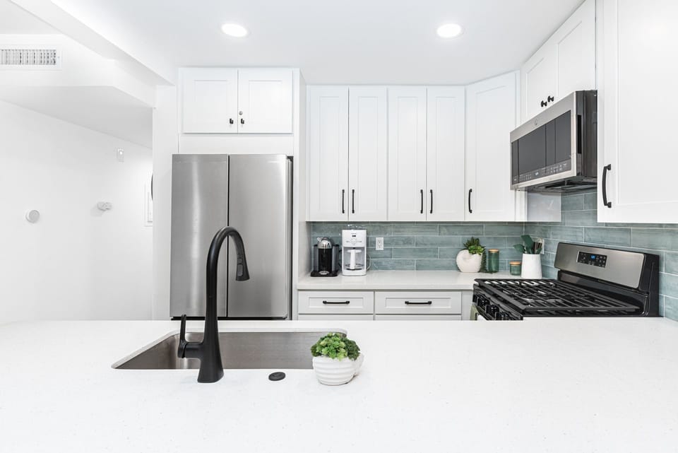 A stylish, contemporary kitchen showcasing bright white cabinetry, pristine countertops, and stainless steel appliances
                