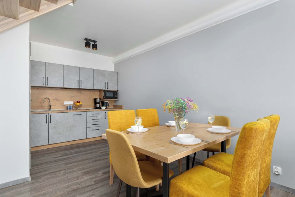 The dining area is set with white plates and glasses, ready for a meal. Behind the table, the kitchen cabinets are finished in a modern grey concrete texture.