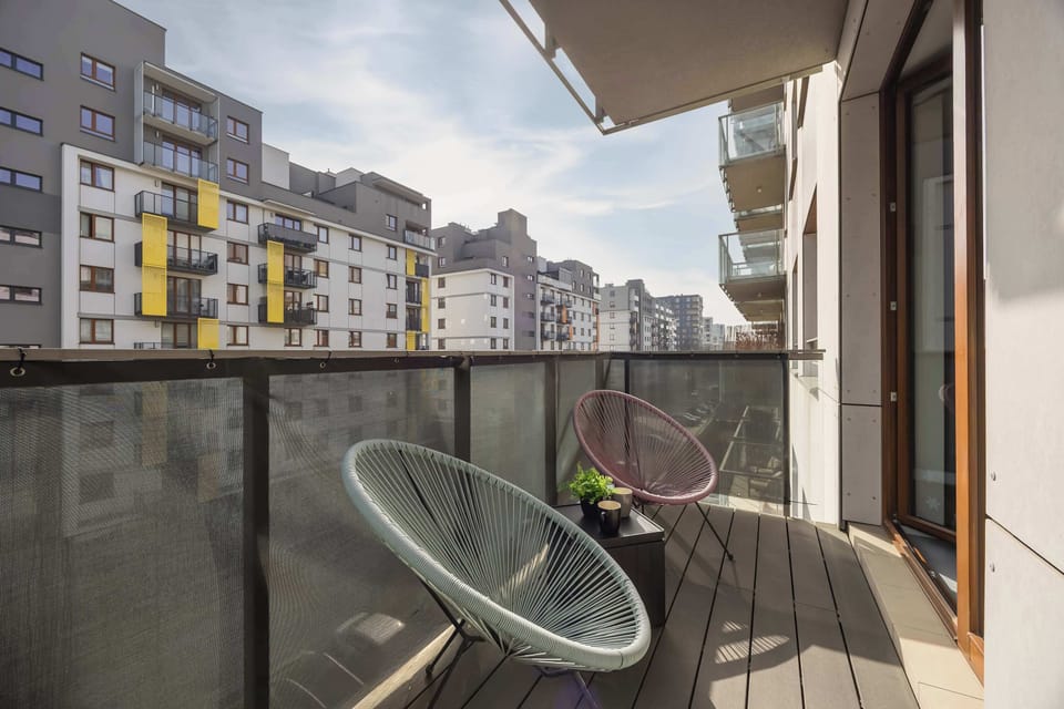 A balcony with a small round table and a chair. The railing overlooks neighboring buildings and outdoor space. It provides a small area for sitting and relaxing outside.