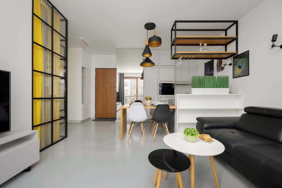 A compact living area with a small table and chairs near the center of the room. Shelving and wall decorations add personality to the otherwise minimalist space. Light-colored floors and walls keep the room bright.