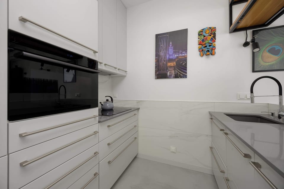 A sleek white kitchenette with built-in appliances including an oven. Cabinets and countertops have a minimalist design. The space looks tidy and functional with a modern style.