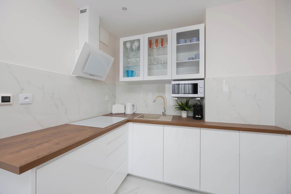A bright kitchenette corner offers minimalist white cabinetry paired with a warm wood-textured countertop and modern built-in appliances.