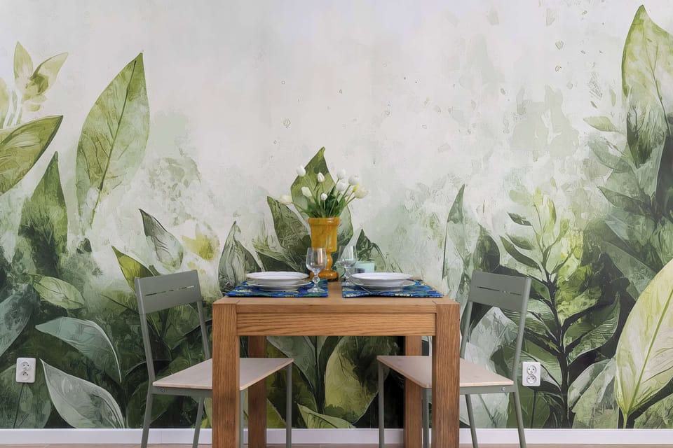 A close view of a dining area with a wooden table and chairs. The wall behind it is covered with large green leaf-pattern wallpaper. Indoor plants and soft lighting add a natural and relaxing feel.