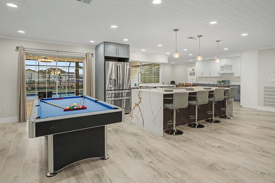 Step into your vacation haven where a sleek kitchen island beckons for morning coffee and evening cocktails, while a pool table invites friendly competition with views of the pool beyond.