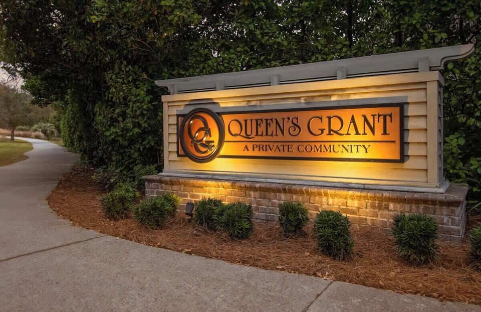 Illuminated entrance sign for Queen's Grant private community, featuring elegant landscaping and welcoming lighting for evening arrivals.