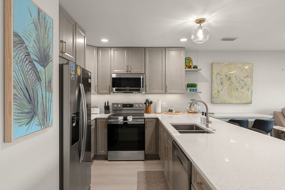 Your fully equipped kitchen awaits with gleaming countertops, stainless steel appliances, and tropical artwork creating a bright, welcoming space for meal prep.