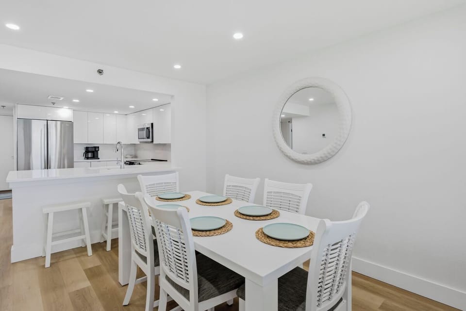 Your modern dining space flows seamlessly into a fully equipped kitchen, where coastal-inspired touches and clean white finishes create the perfect setting for memorable meals.