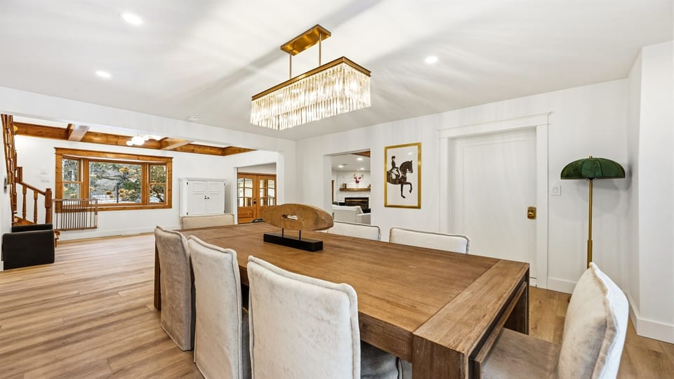 The dining table comfortably seats 8, with modern, rustic touches, the space is bathed in natural light from the large windows, creating a warm and inviting atmosphere.