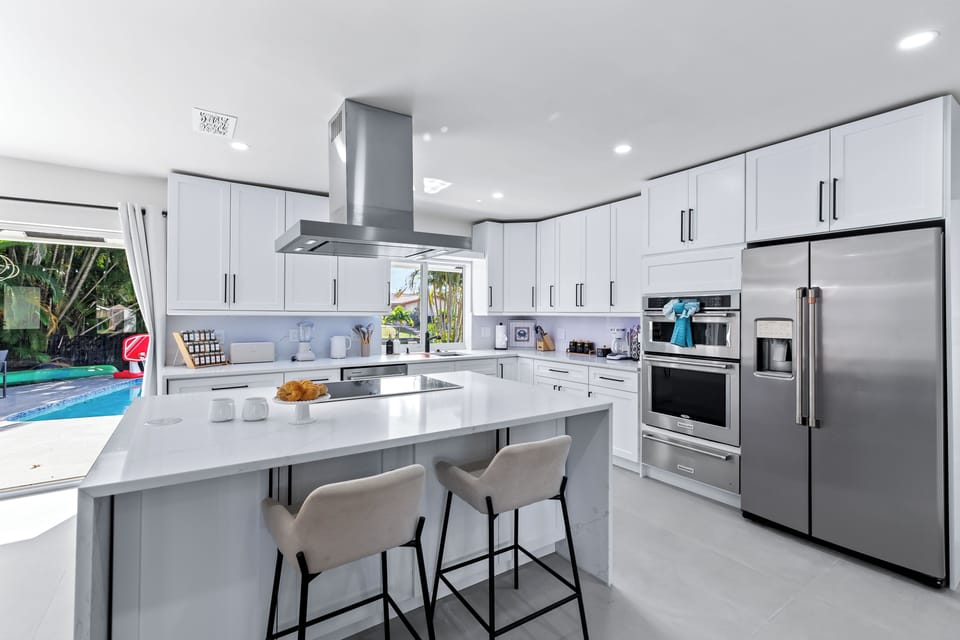 Sleek, chef-ready kitchen with a huge island and bar seating—stocked with stainless steel appliances and steps from the pool for effortless indoor-outdoor living.