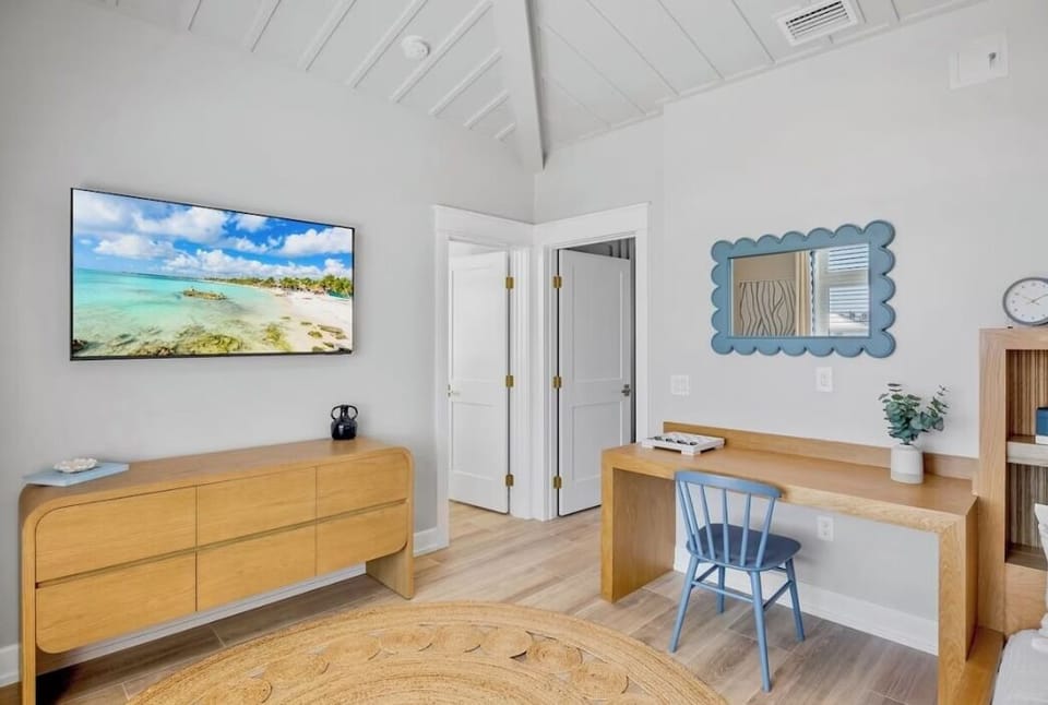 Your bright workspace awaits with warm wood desk, coastal TV, and vaulted ceilings creating the perfect blend of productivity and relaxation.