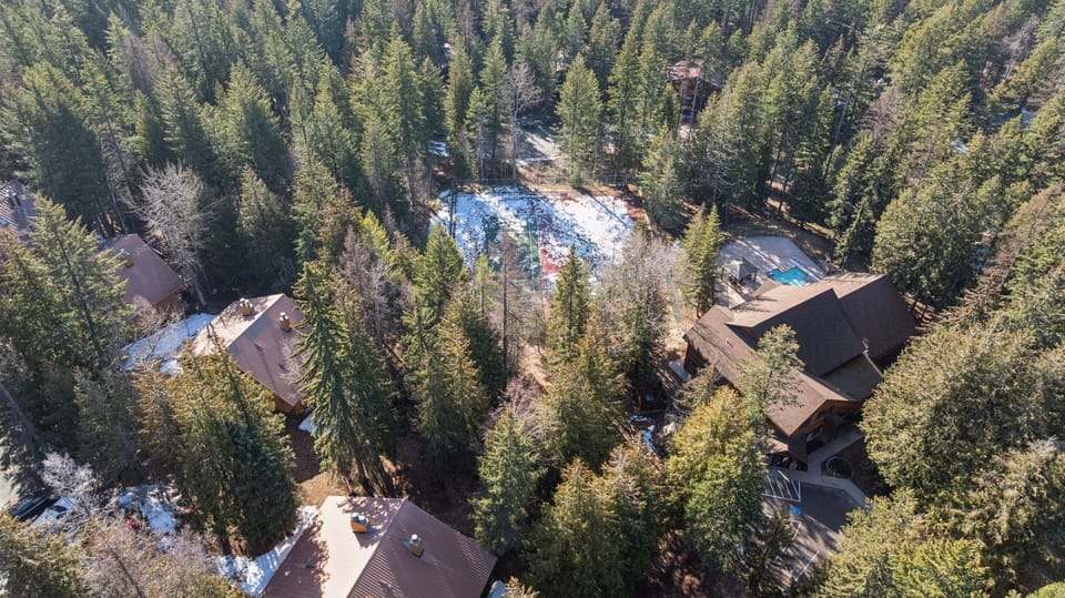 Aerial view of mountain resort property nestled among towering evergreen trees with swimming pool and recreational facilities.