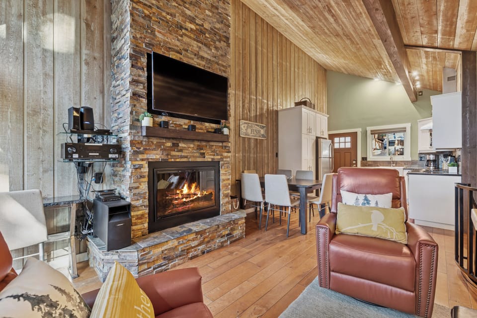 Relax in your rustic-chic living space featuring a stone fireplace, vaulted wood ceilings, and leather seating perfect for cozy evenings.