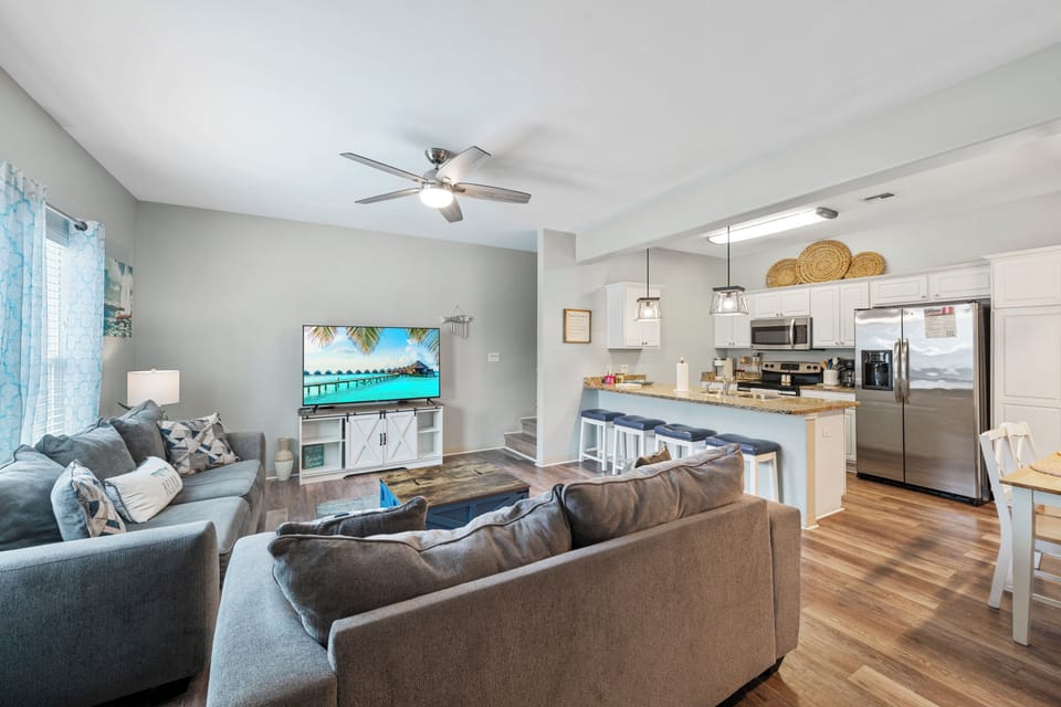 Sink into plush sofas in your open-concept living space, where coastal vibes meet modern comfort with a fully-equipped kitchen perfect for family gatherings.