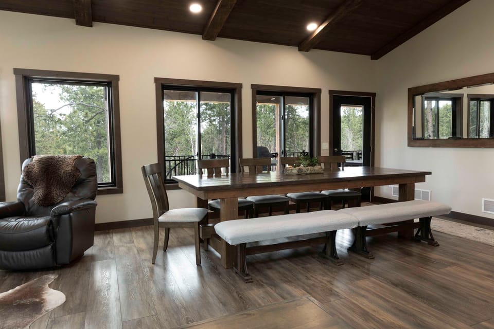 Large dining table at Quittin’ Time with forest views through tall windows and easy access to the deck. Plenty of space for big dinners, morning coffee, and planning the next Black Hills adventure.