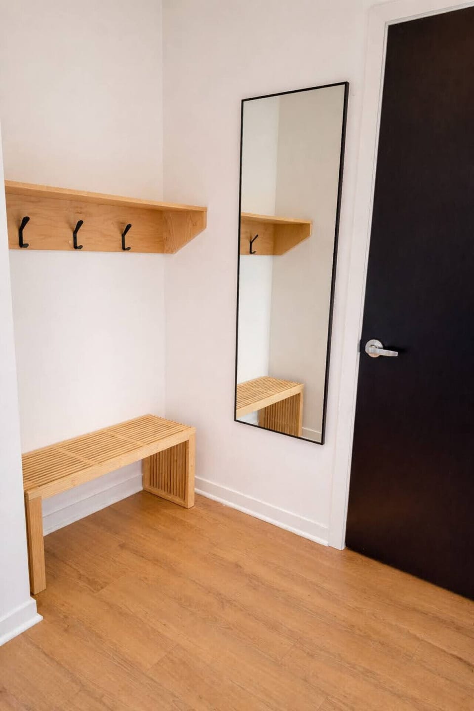Convenient and minimalist entryway with a natural wood bench, wall hooks, and full-length mirror—perfect for dropping bags and getting ready to head out