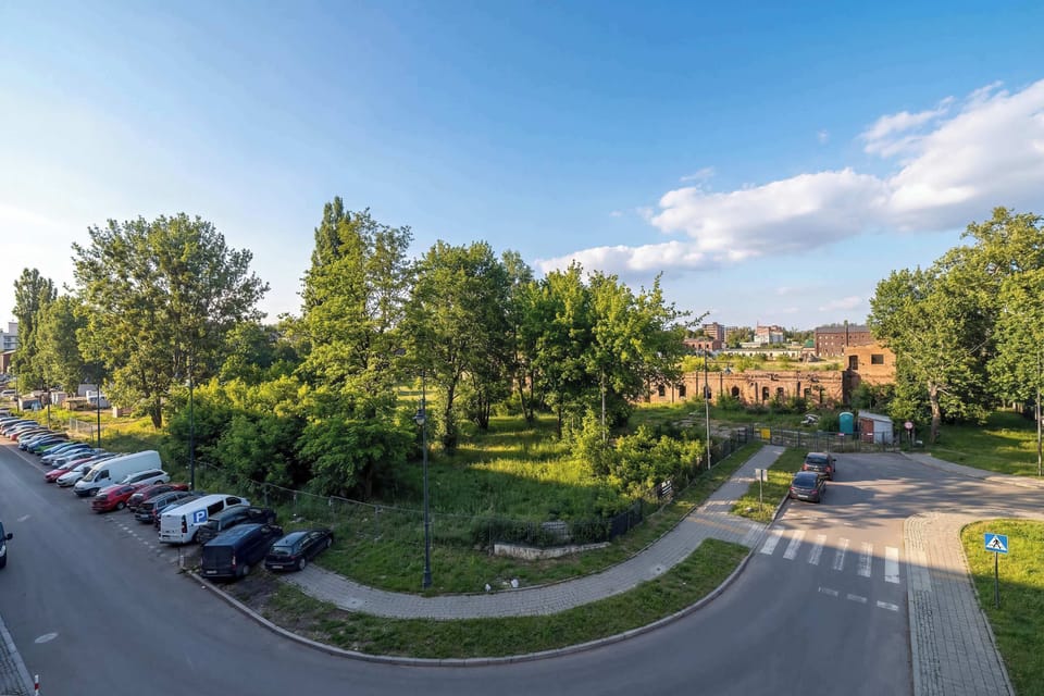 A panoramic street view with green trees, sidewalks, and residential buildings. The sunny weather and blue sky give the neighborhood a pleasant atmosphere.