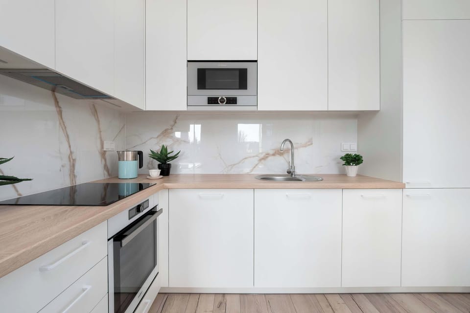A modern kitchenette with white cabinets and built-in appliances. The countertop is tidy with minimal decorations, emphasizing a clean design.