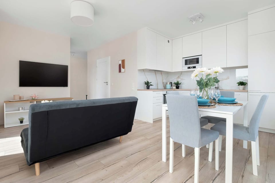 A view of the living room and dining space from another angle. The open layout connects the kitchenette, dining table, and sofa in a bright shared area.