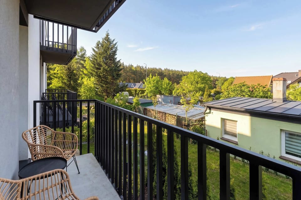 A balcony view overlooking nearby residential buildings, trees, and a quiet neighborhood street under a clear sky.