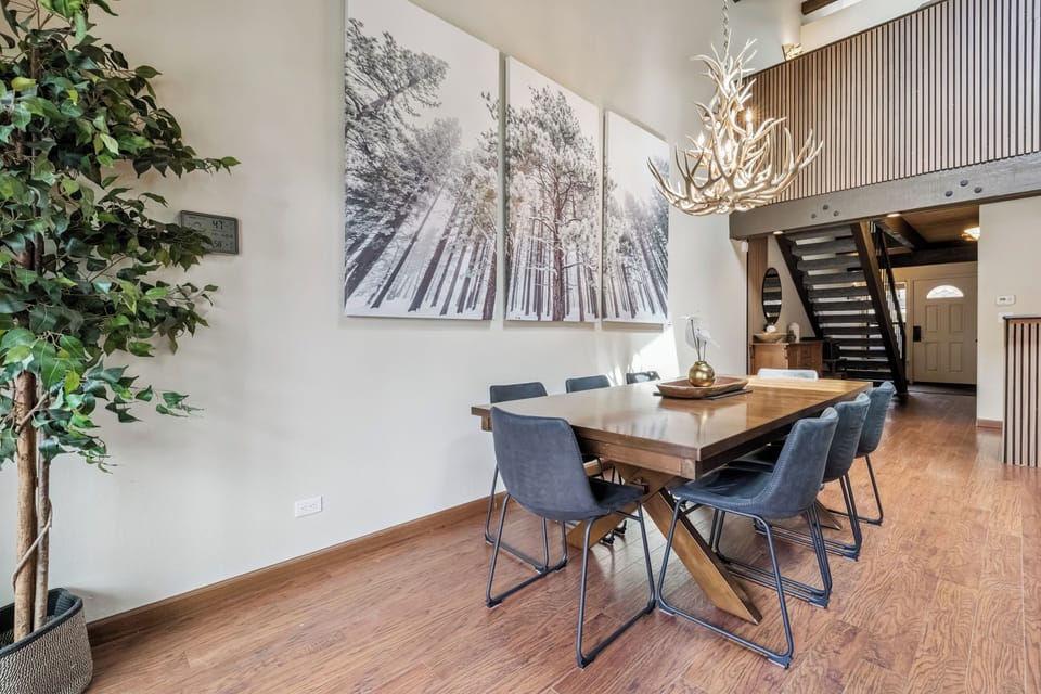 Gather around this warm wooden dining table under a rustic antler chandelier, where your group can share meals and make memories in this inviting mountain-inspired space.