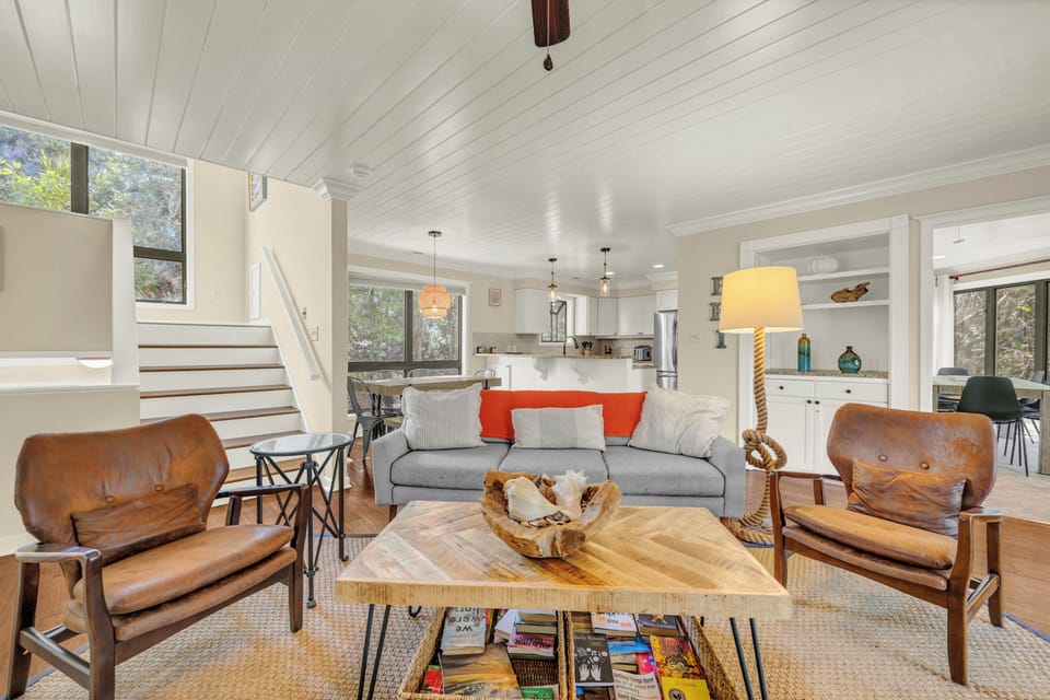 Sink into plush seating in this bright, open living space where coastal charm meets modern comfort. Natural light streams through large windows, highlighting the vaulted shiplap ceiling and ocean-inspired accents.
