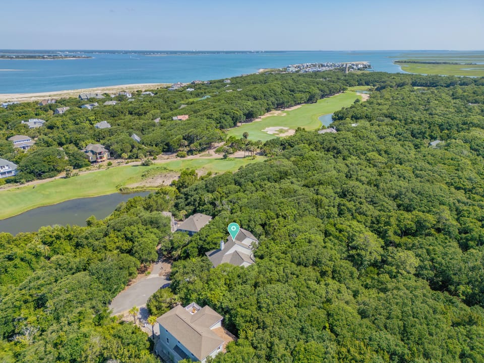 Aerial view showcasing a coastal property nestled among lush greenery, with golf course fairways, nearby beaches, and serene ocean waters defining the surrounding area.