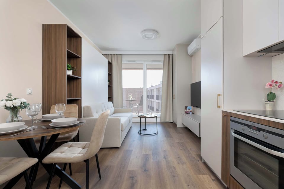 A long view of the open kitchen and dining area reveals a bright window at the far end. Wooden floors and white walls create a balanced interior.