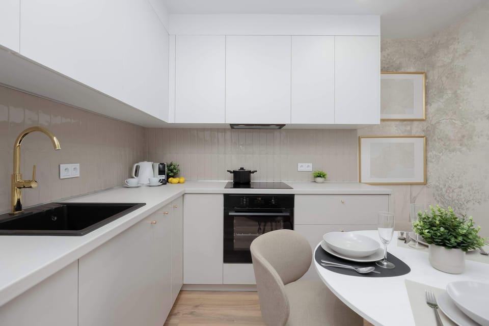 A sleek, modern kitchen is equipped with a dark countertop, an integrated stovetop, and clean white upper cabinets. A small dining setup with a potted plant adds a touch of freshness to the culinary space.