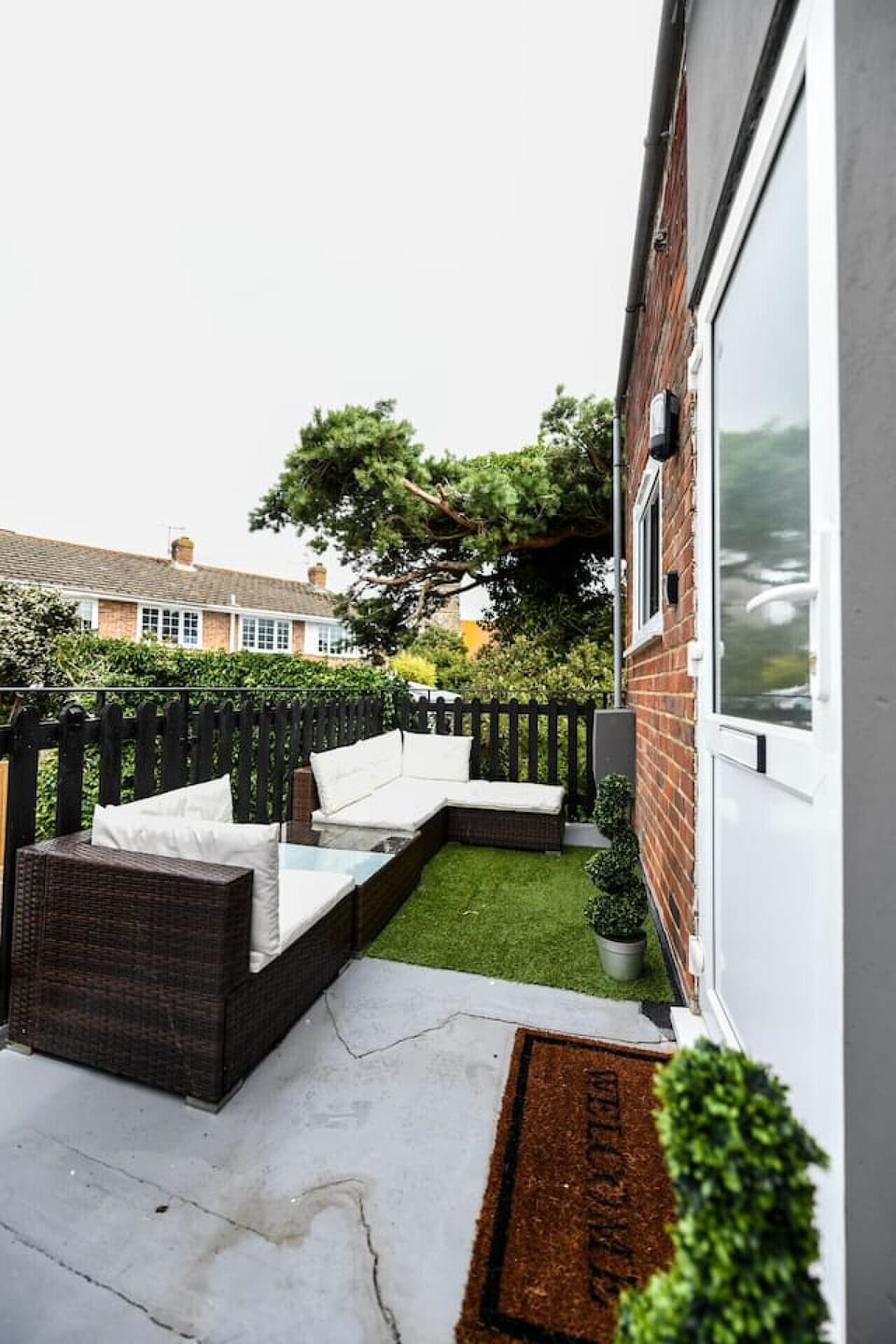 An outdoor seating area with white bench seating, a raised planting border, a timber-decked section, and a brick boundary wall with greenery above.