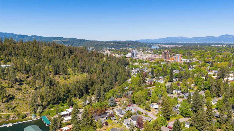 Aerial view capturing the scenic surroundings near the property, framed by lush forests, rolling mountains, and a peaceful lakeside area at the property's edge.