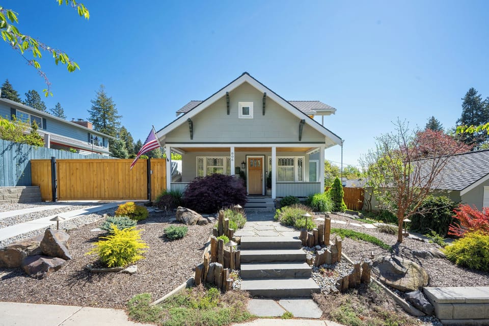 Charming craftsman-style home with welcoming front porch, landscaped garden, and serene residential setting under clear blue skies.