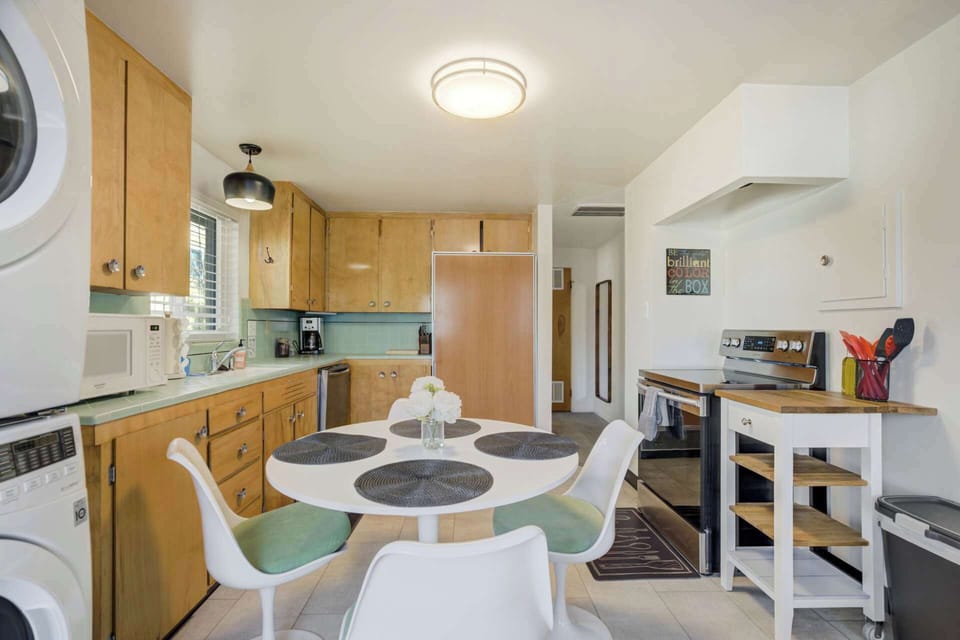 Cook and connect in the open kitchen—warm wood cabinets, a full stove, and a round dining table with modern chairs ready for pancakes or takeout nights.