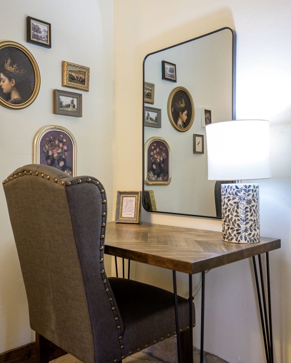 A compact desk with upholstered chair, lamp and large mirror provides a dedicated work area.