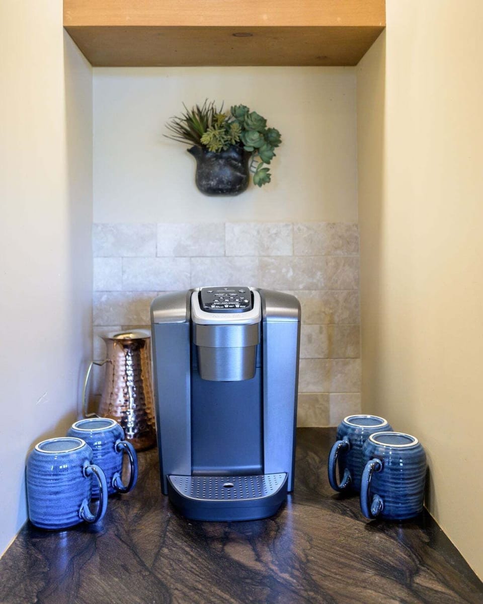 A single-serve coffee maker and four mugs are arranged in a recessed beverage nook.