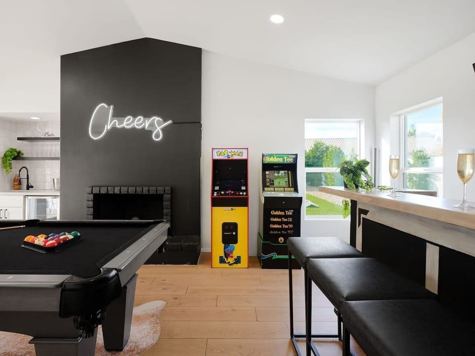 Game room featuring a pool table, wet bar with a mini fridge, arcade games, a smart TV with bar seating, and backyard access.