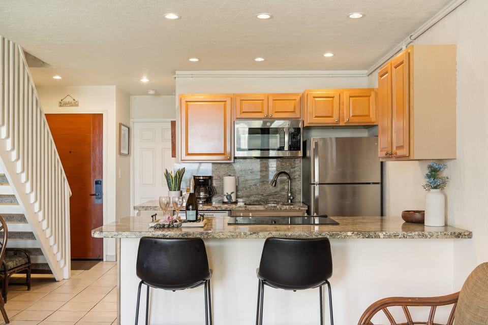 Modern kitchen featuring granite countertops, stainless steel appliances, warm wood cabinetry, and a cozy breakfast bar.
