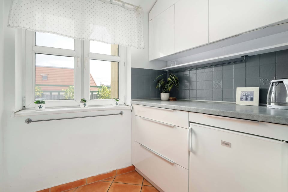 A compact kitchen with white cabinetry, gray backsplash tiles, and a window bringing in natural light.