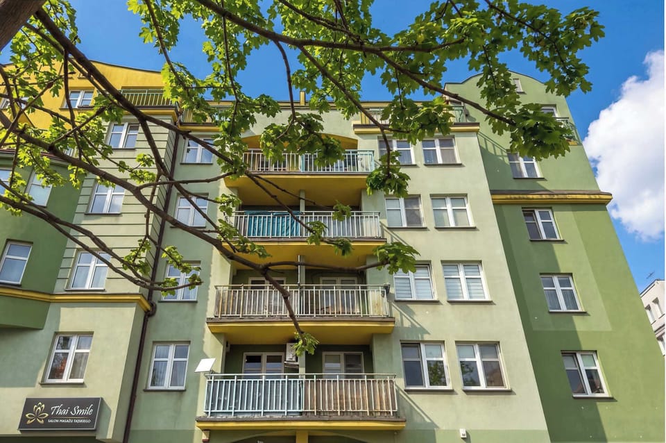 A view of a green apartment building with balconies and trees in front, seen from below.