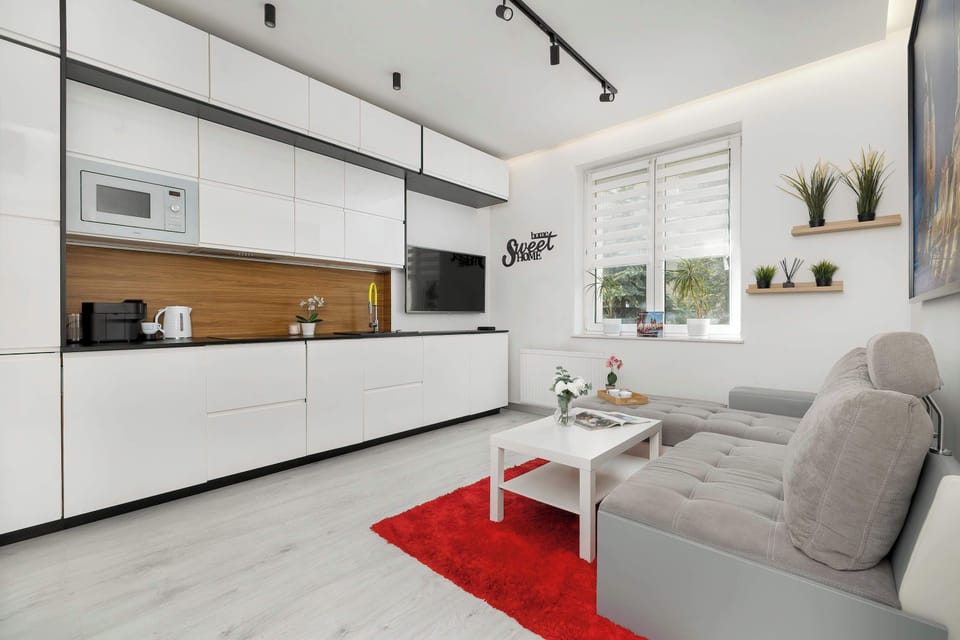 A wide view of the entire living room, featuring visible track lighting on the ceiling and a light-colored floor. The space is organized, bright, and ready to welcome its first guests.