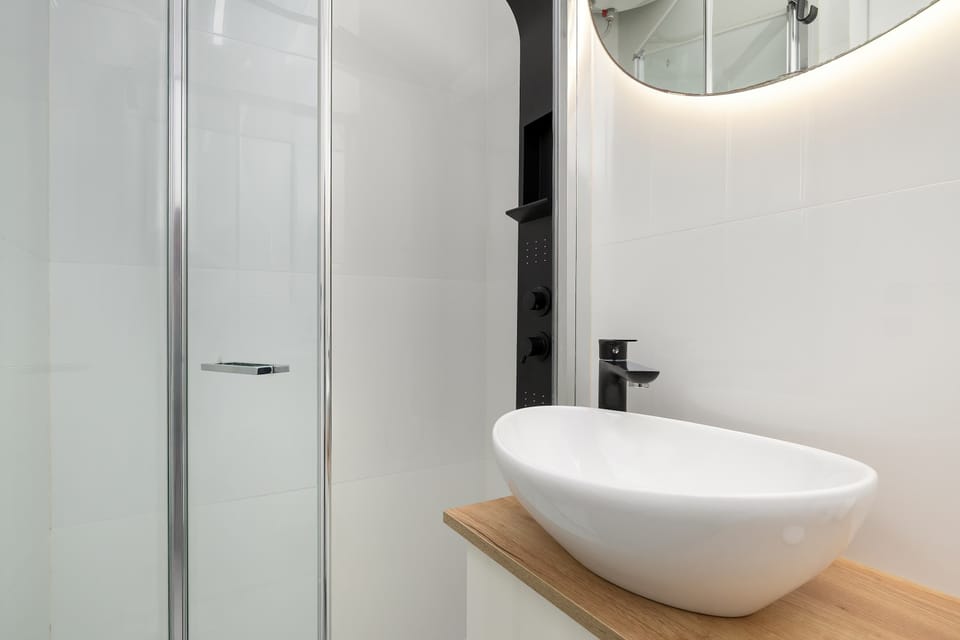 A shower enclosure with clear glass and modern black fixtures, including a rain showerhead. The interior of the shower is finished with white tiles, which enhances the impression of immaculate cleanliness.