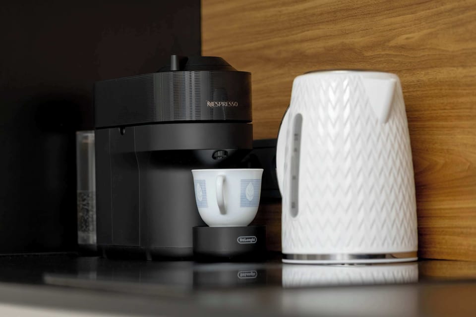 A close-up of the kitchen appliances, including a modern coffee maker and a white electric kettle with an interesting texture. The appliances are set on a dark countertop against a warm, wooden finish.