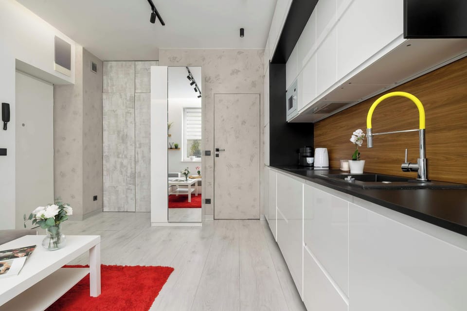 A view from the entryway toward the kitchenette, showcasing a yellow designer faucet that serves as an energetic pop of color against the black-and-white cabinetry. On the left, doors leading to the other rooms are visible.