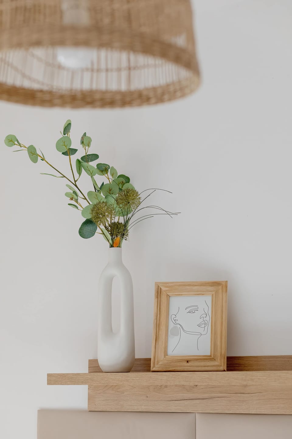 A simple wooden bedside table holds a white vase with green leaves and a small wooden frame. This minimalist styling contributes to the overall clean and organized feel of the bedroom.