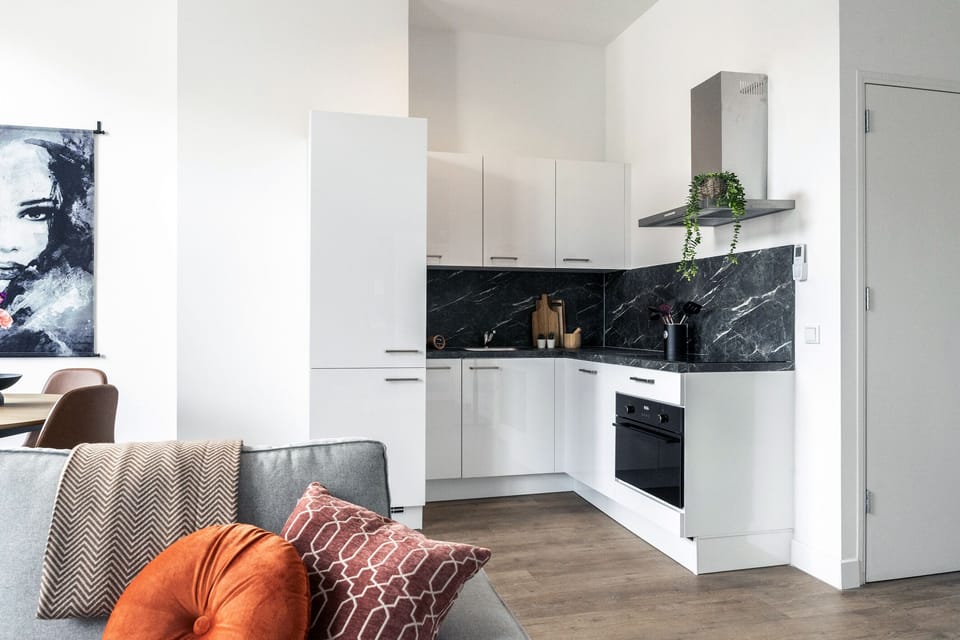 Sleek white kitchen with black marble backsplash, built-in appliances, and open layout flowing into a cozy living area with warm-toned accents.