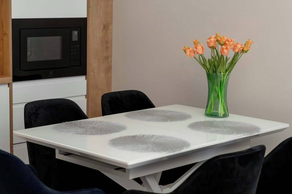 A compact dining table with black chairs and a small vase of flowers on top. The arrangement is neat and practical. The space feels intimate and functional.